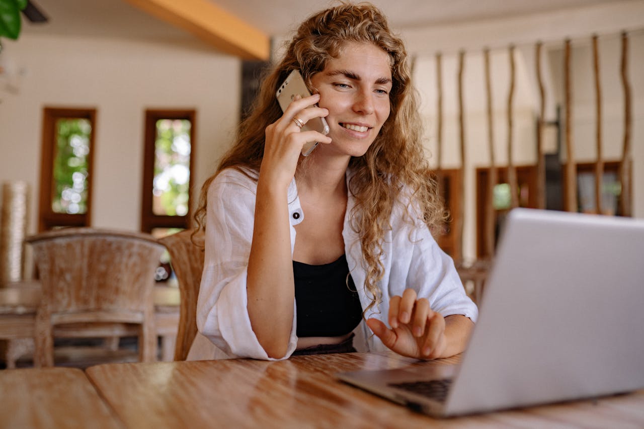 Smiling woman working remotely with a laptop and phone in a cozy setting.